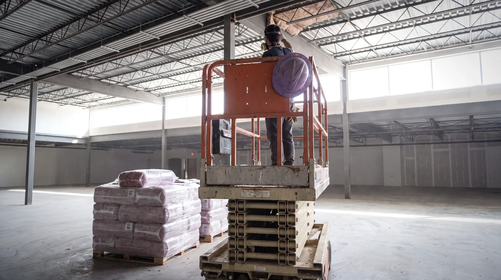 Commercial insulation being installed from a lift in a warehouse